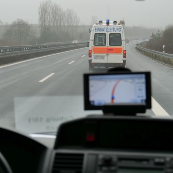 Blick aus dem Fenster eines Einsatzfahrzeuges: Vorne fährt ein Kleinbus mit der Aufschrift Einsatzleitung auf einer nassen Straße.