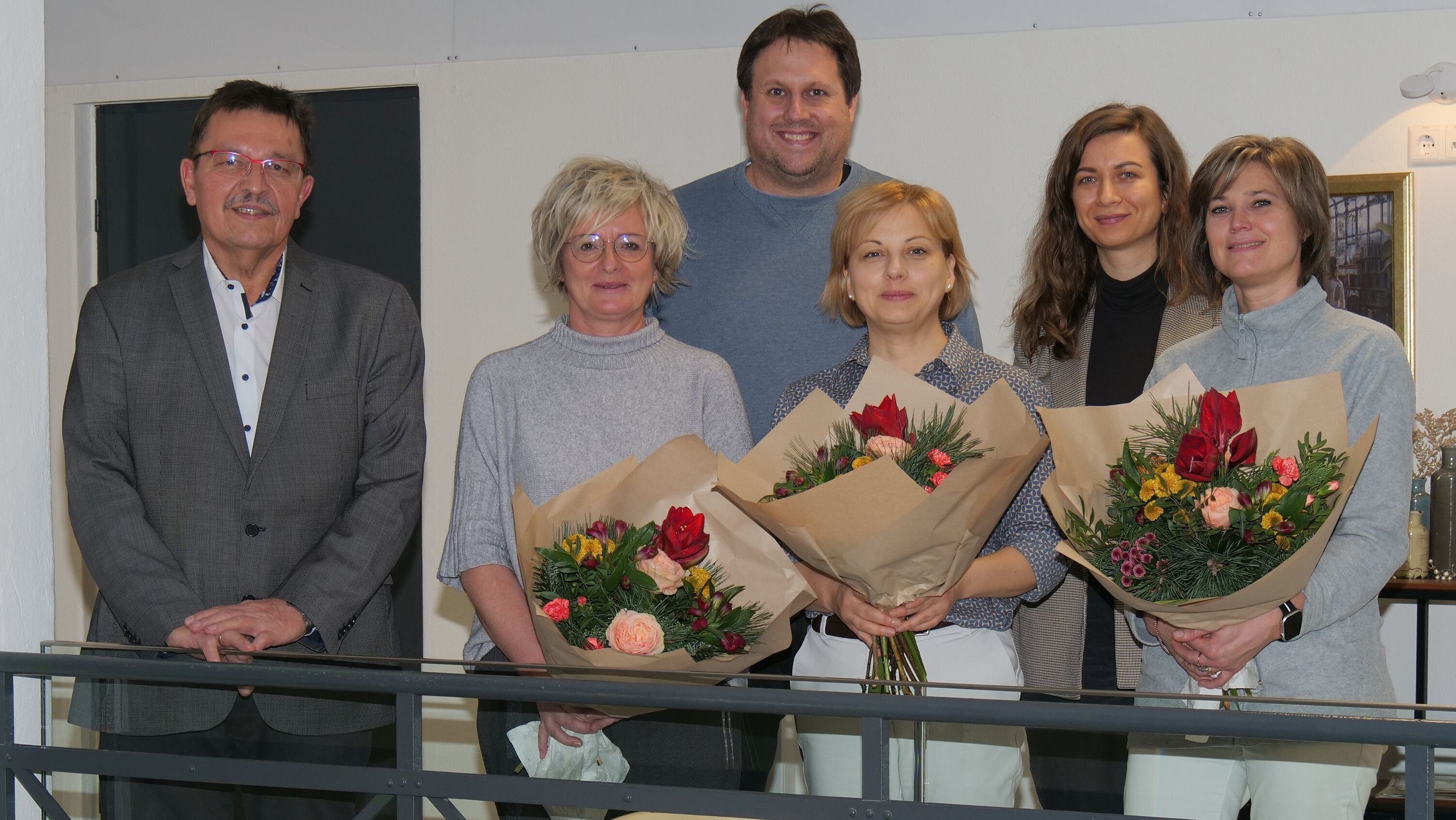 Jürgen Wittmann, Claudia Angermüller, André Dehler, Anastasia Patuk, Jennifer Schneider und Eugenia Wagner-Pochlebaev stehen mit Blumensträußen in den Räumen der neuen Arztpraxis in Grub am Forst.