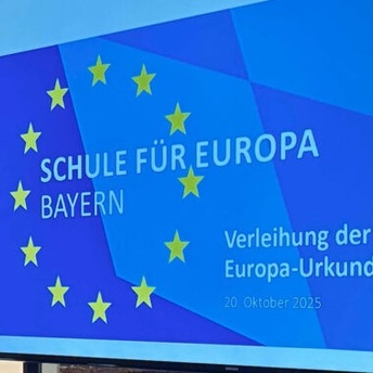 Ein Bildschirm, auf dem in gelber Schrift auf blauem Untergrund steht: Schule für Europa, Verleihung der Europa-Urkunde