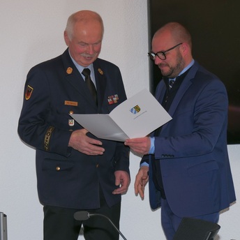 Landrat Sebastian Straubel überreicht an Reinhard Hartung eine Urkunde des Freistaats Bayern.