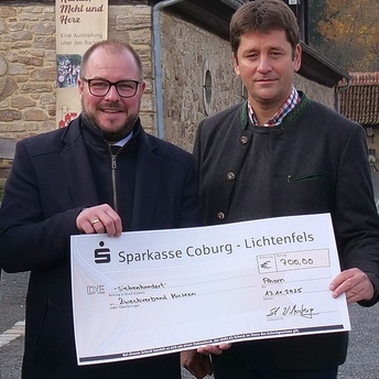 Landrat Sebastian Straubel und Stefan Wittenberg halten gemeinsam einen großen Scheck über einen Betrag von 700 Euro in der Hand.